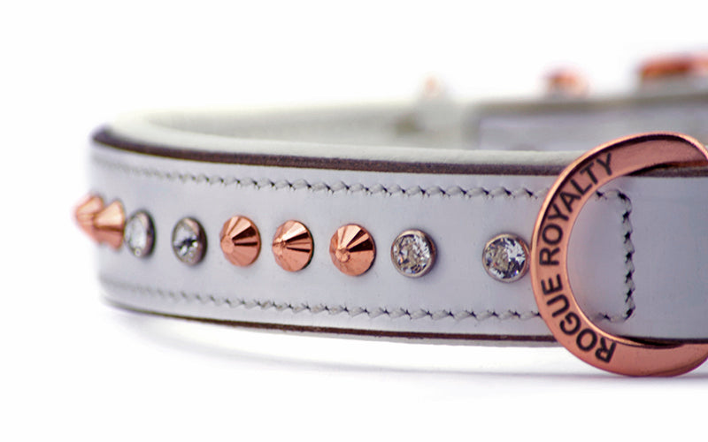 Close up view of Swarovski crystal rhinestones and rose gold hand carved studs set into a white leather dog collar.
