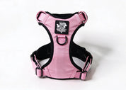 Pink and black dog harness with a central logo patch, photographed on a clean white background.